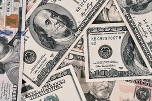 Fajos de dólares sobre una mesa con billetes argentinos de fondo